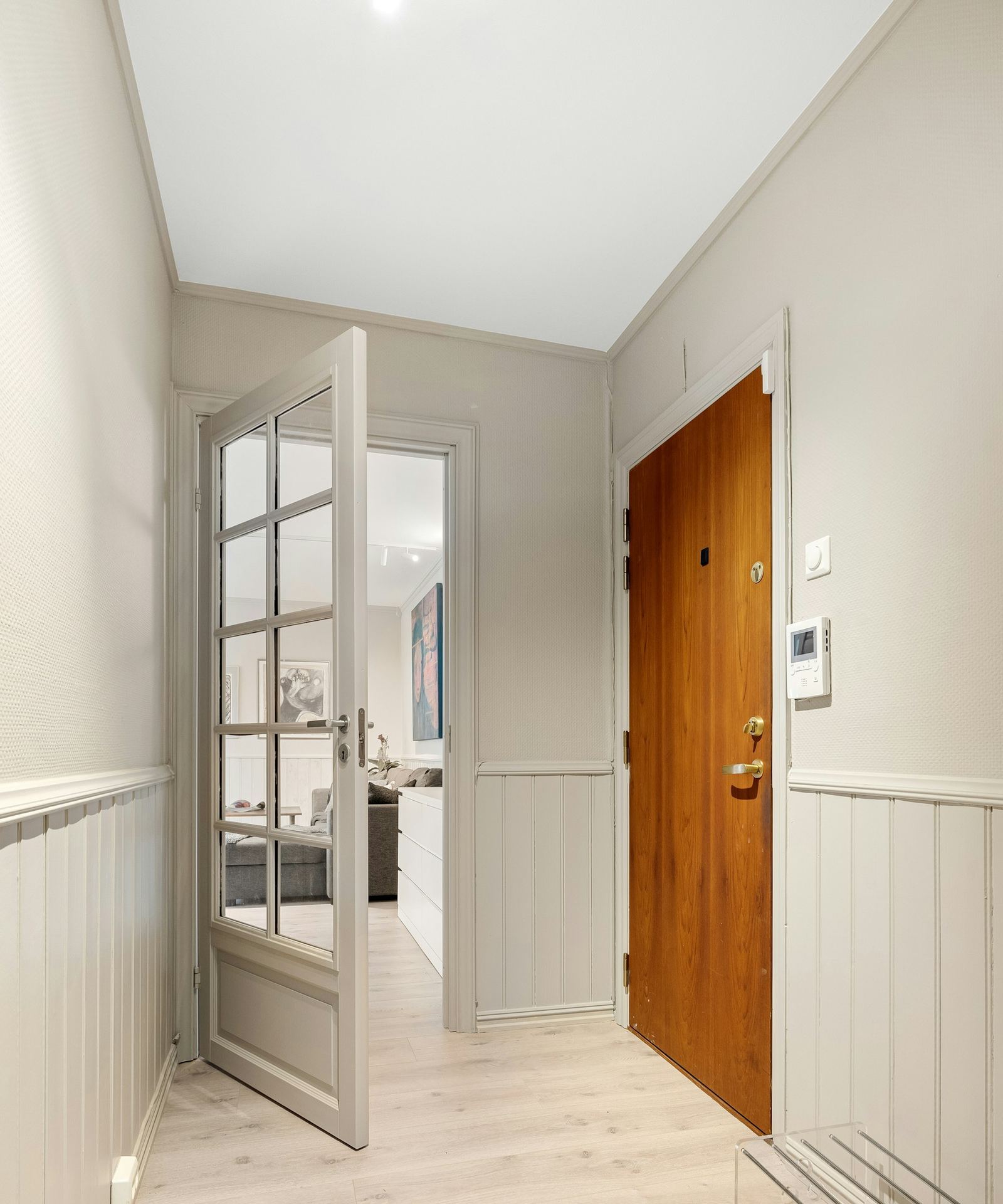 Hallway with an open glass panel door, a wood door, and painted wainscoting