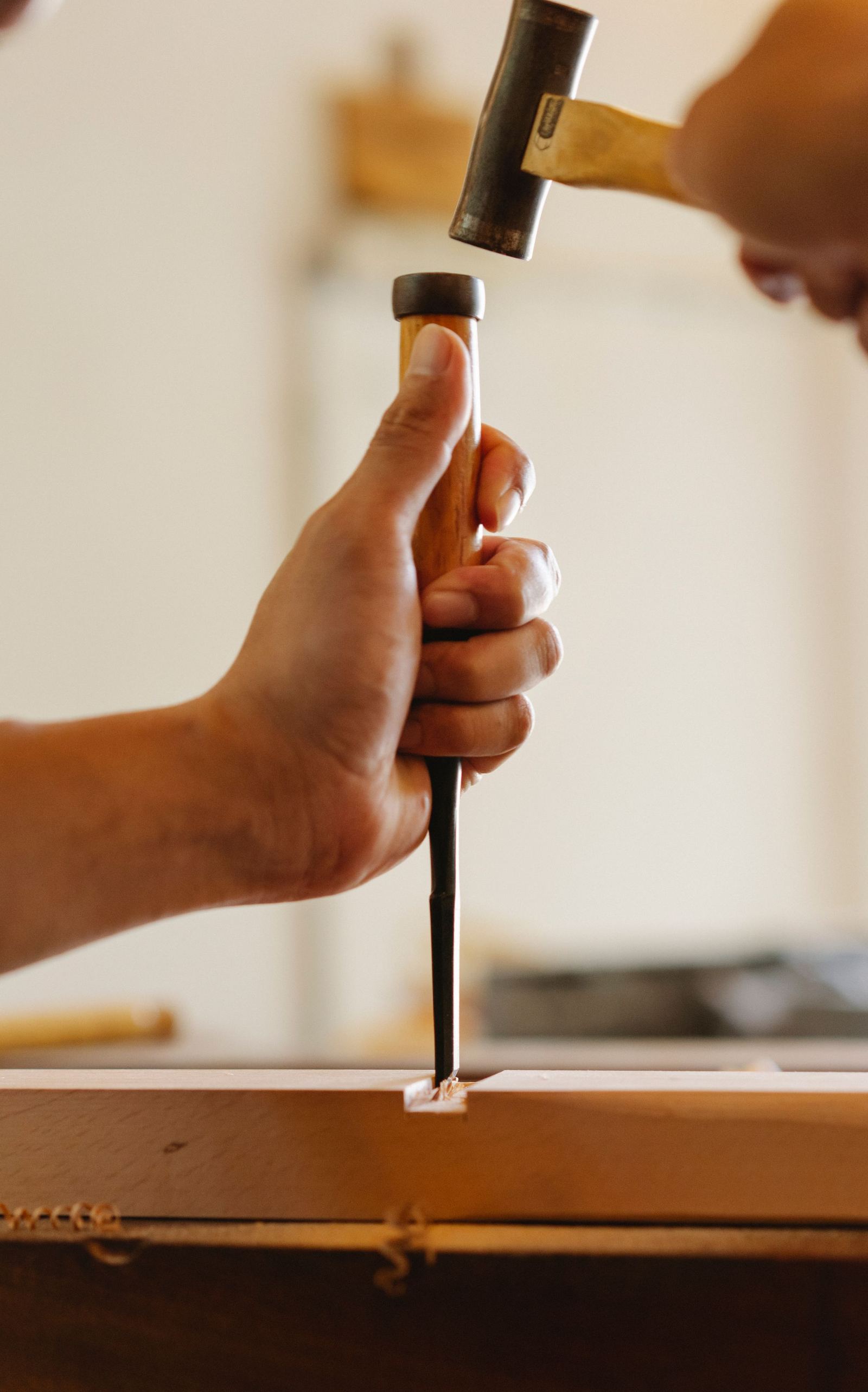 Hands using a hammer and chisel to cut a joint in a wood board